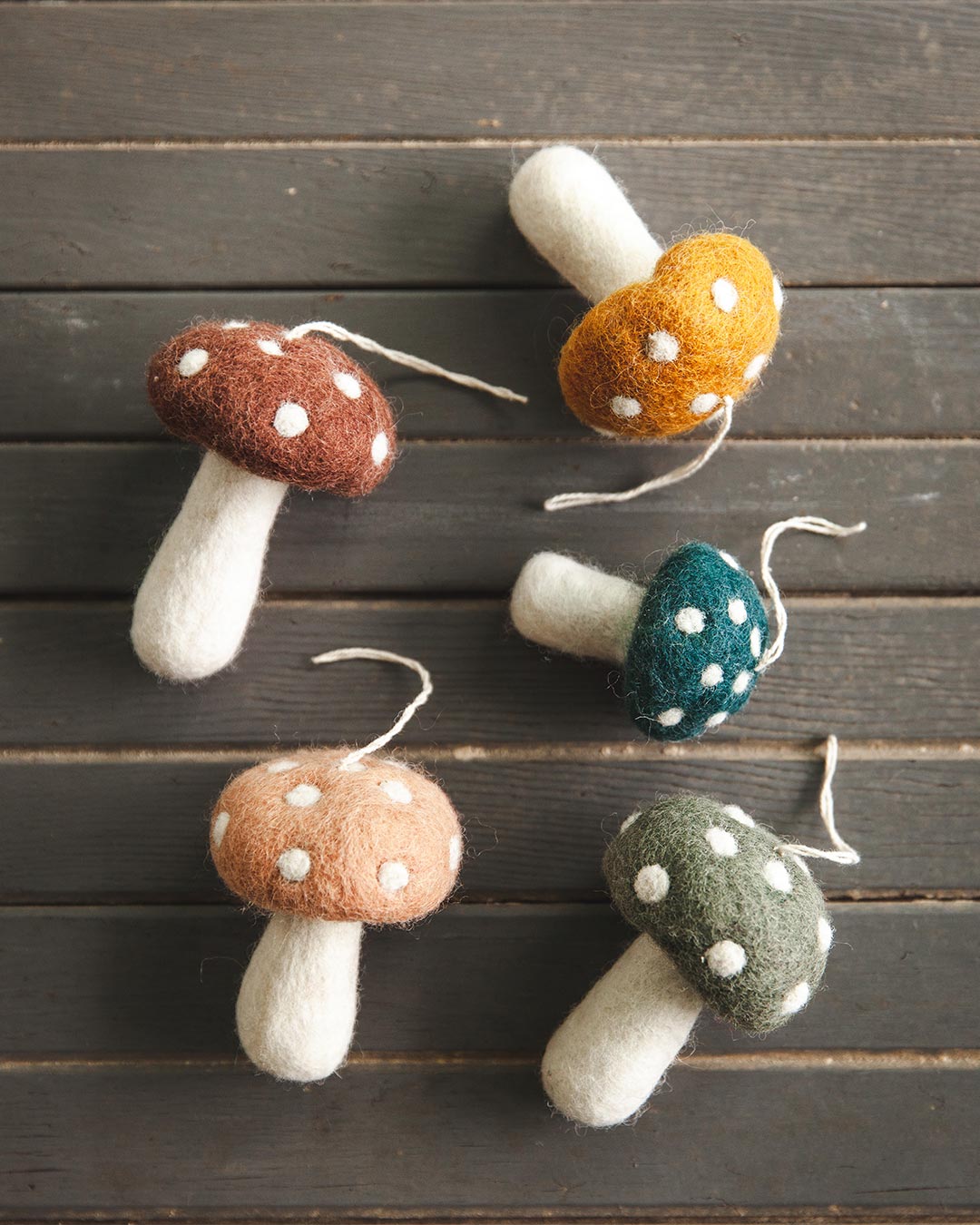 Farmhouse Pottery felted mushroom ornaments in all colors laying on wood floor.