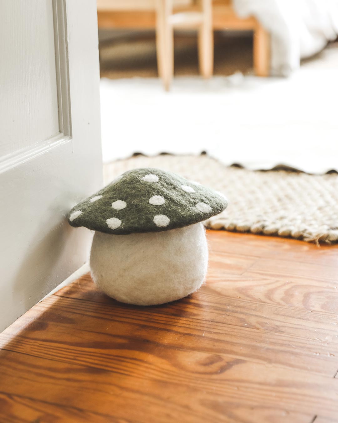 Farmhouse Pottery artisan felted mushroom doorstop in moss holding door open. 