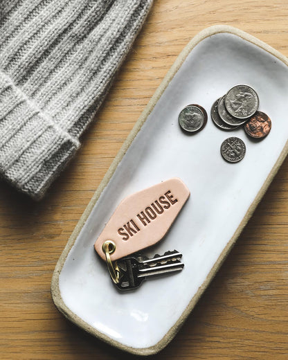 Farmhouse Pottery Ski House happy place keychain in tray with keys and coins. 